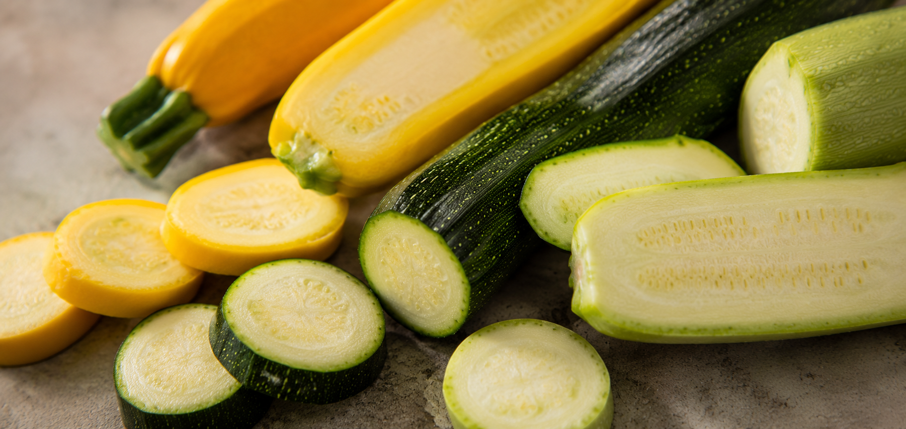 Yellow and green zucchini, both whole and sliced, are arranged on a light surface—perfectly prepped to showcase their vibrant colors and fresh textures. An ideal display of ingredients ready for precision cutting or cooking in high-quality Fissler stainless steel cookware, where innovative design meets timeless German craftsmanship.