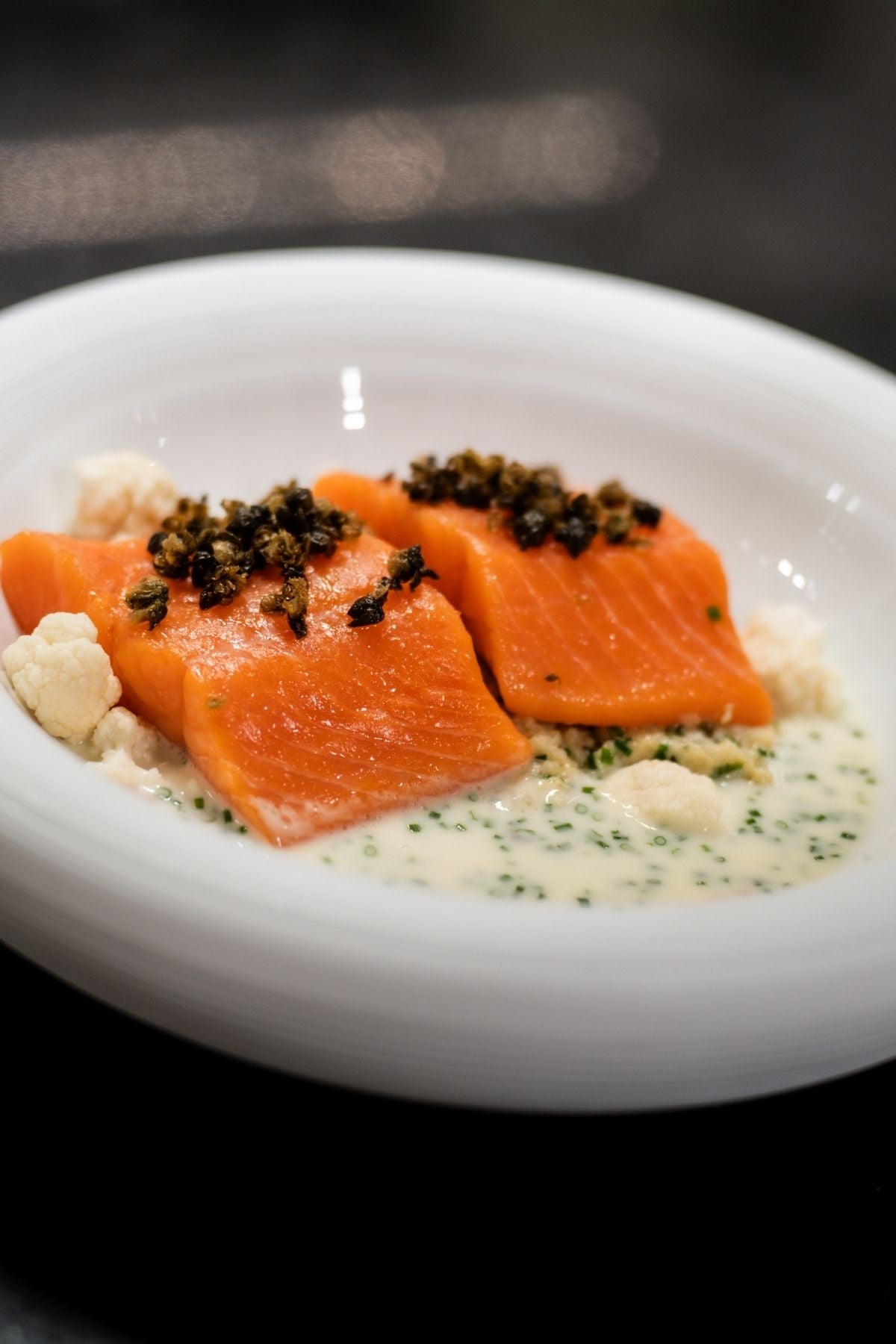 Perfectly cooked salmon with capers and cauliflower on a creamy herb sauce, elegantly served in a white bowl - in Fissler quality.