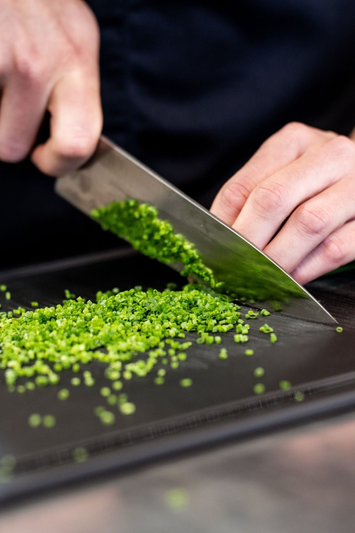 A person chops fresh green herbs on a dark board, showcasing the precision of a high-quality Fissler kitchen knife.