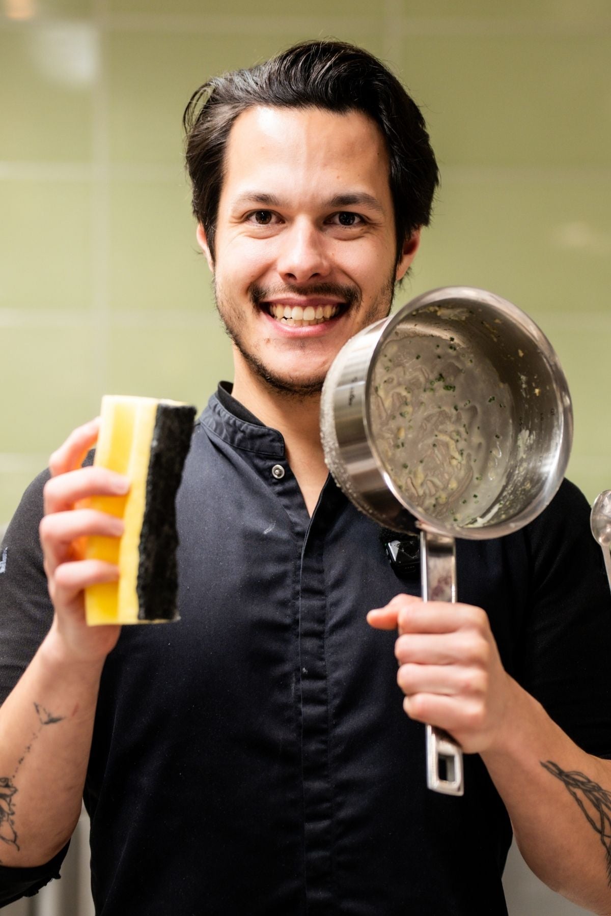 A smiling chef in uniform stands in a modern kitchen, ready to clean a Fissler pot, symbolizing German quality and innovation.