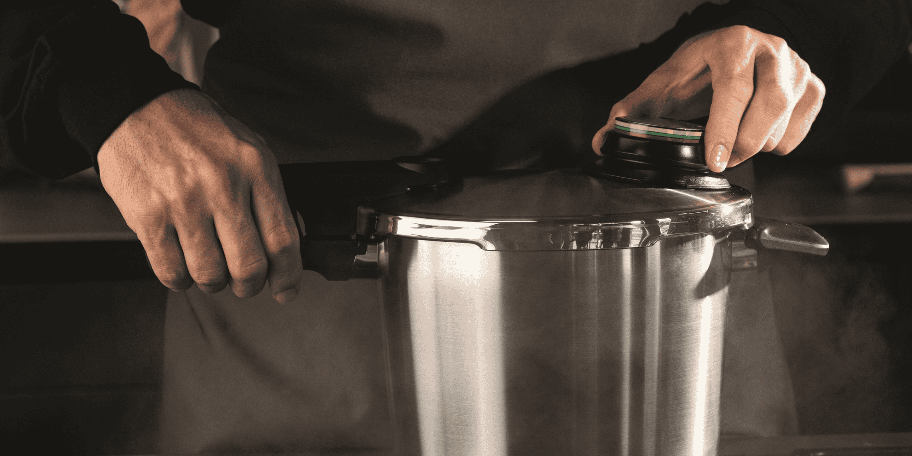 Hands operate the lid of a stainless steel Fissler pressure cooker, releasing steam in a modern kitchen and demonstrating German precision.