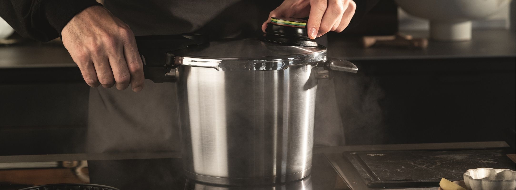 Eine Person öffnet einen Fissler Schnellkochtopf aus Edelstahl und lässt Dampf auf einer Küchentheke ab - deutsche Präzisionsarbeit in Aktion.