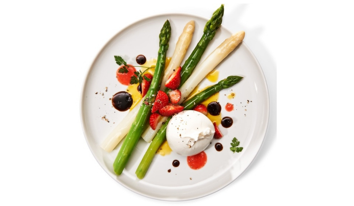 Asparagus, strawberries, burrata, and herbs are presented on a white plate - prepared with Fissler cookware for perfect precision and style.