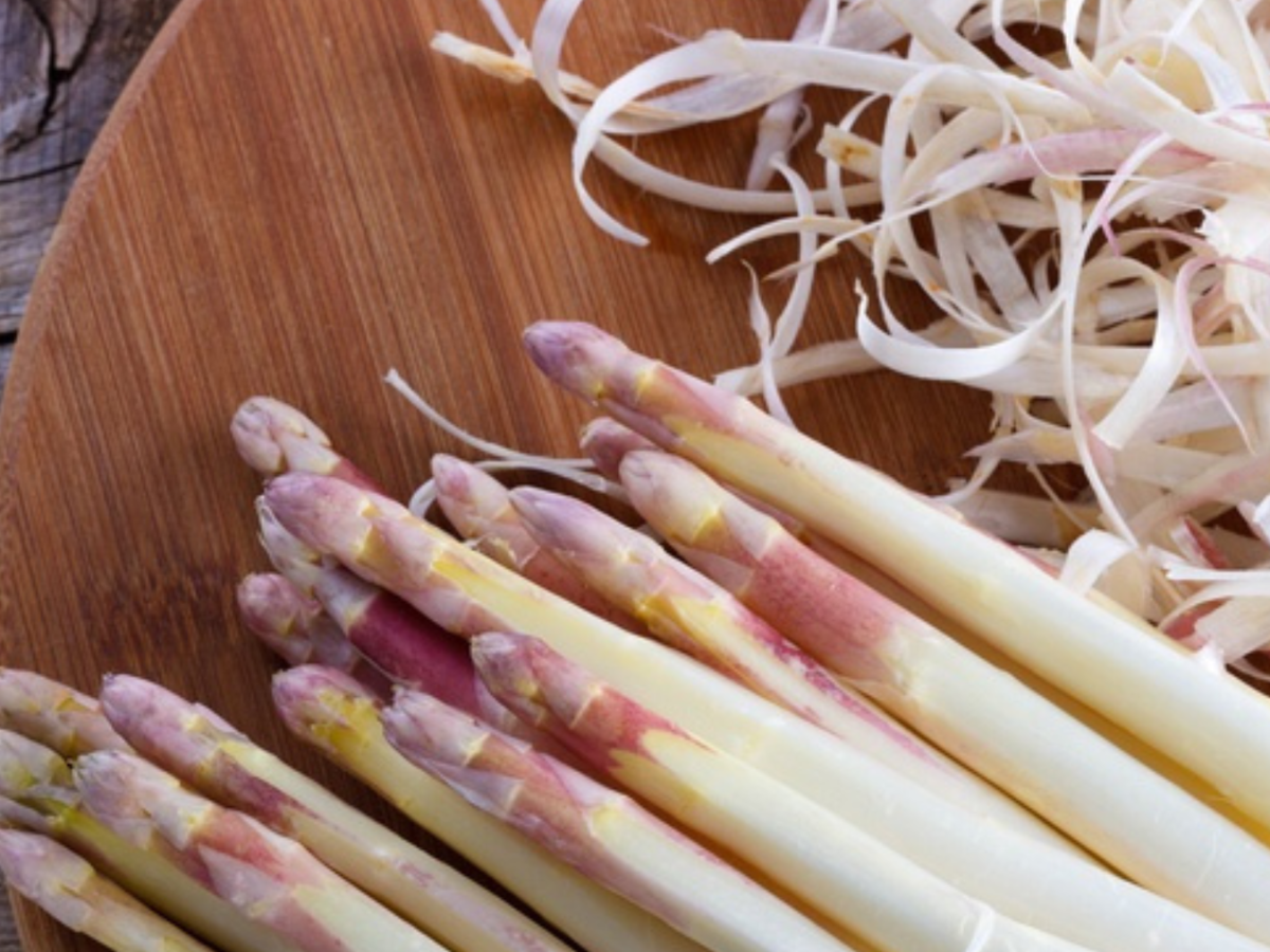 Weißer Spargel mit violetten Spitzen liegt neben den Schalen auf einem Holzbrett, zubereitet mit Fisslers präzisen deutschen Küchengeräten.