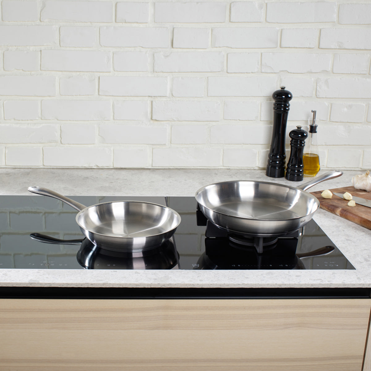 Fissler Catania Pfannenset (24/28 cm) für Induktionskochfelder, mit Salz- und Pfeffermühlen, Öl, Knoblauch und Holzbrett.