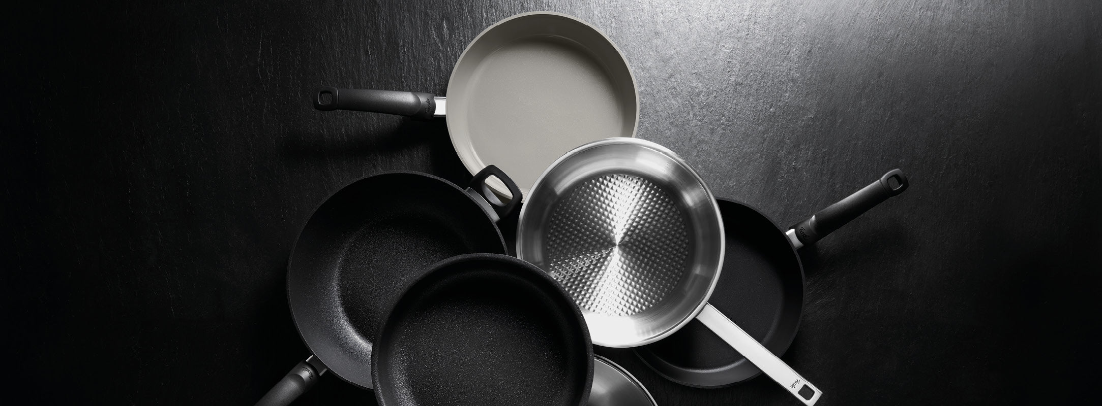 Ein Kreis von sechs Fissler Bratpfannen in hochwertigen Ausführungen, die deutsche Präzisionsarbeit und zeitloses Design präsentieren.