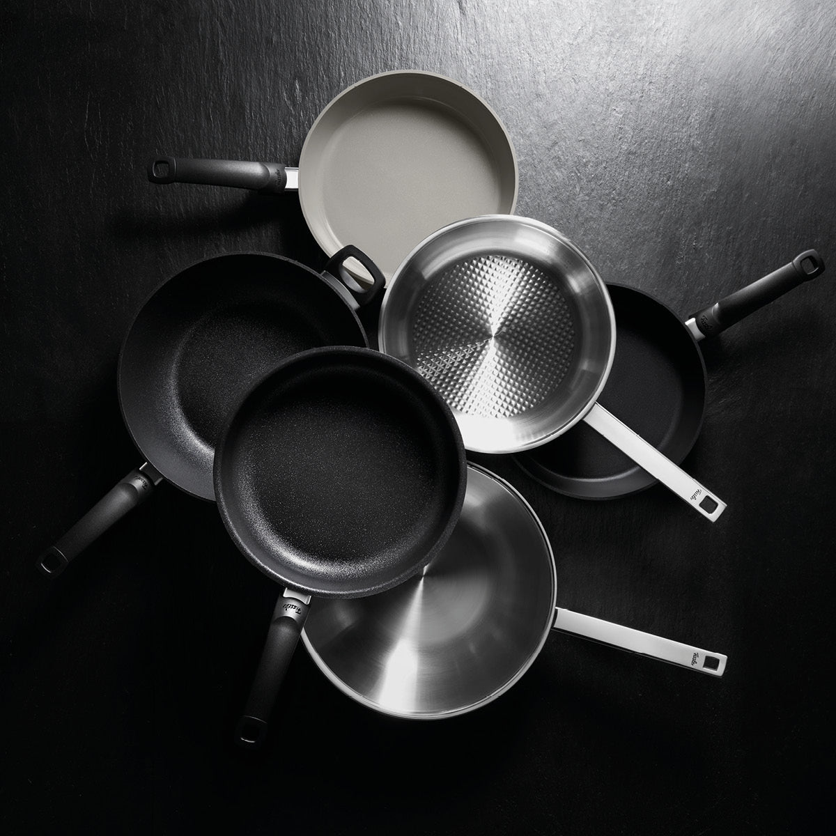 Sechs hochwertige Fissler Bratpfannen aus Edelstahl und mit Antihaftbeschichtung strahlen nach außen und präsentieren Präzision und zeitloses deutsches Design.