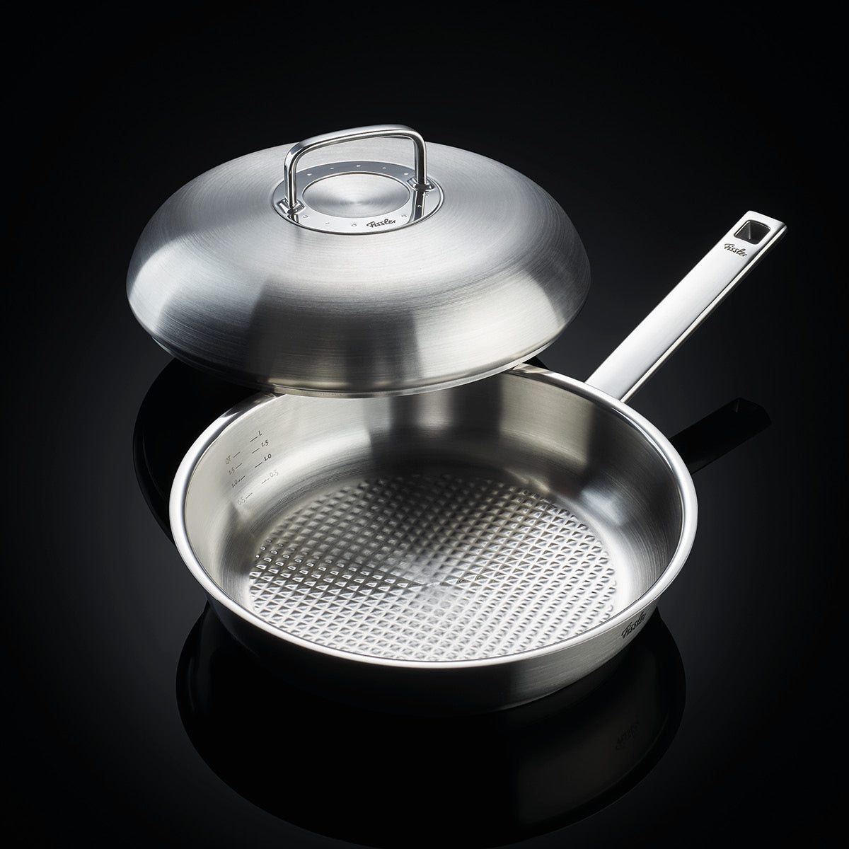 Fissler Bratpfanne aus rostfreiem Stahl mit der charakteristischen strukturierten Innenseite und einem Präzisionsdeckel, der leicht geneigt ist, um die deutsche Qualitätsarbeit zu zeigen.