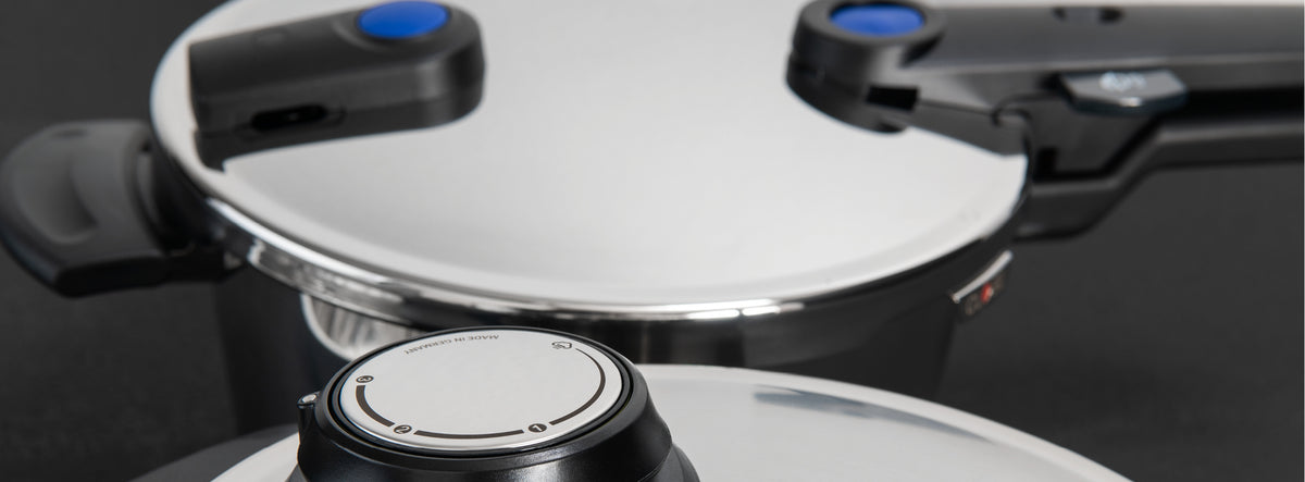 Nahaufnahme von zwei Fissler Schnellkochtopfdeckeln aus Edelstahl mit ergonomischen schwarzen und blauen Griffen, die deutsche Handwerkskunst demonstrieren.