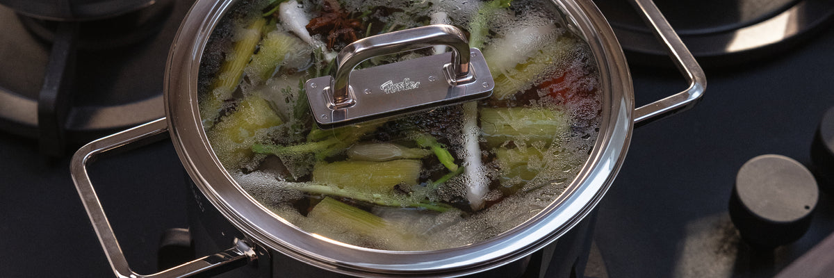 Ein Fissler-Edelstahltopf mit Glasdeckel dünstet frischen Lauch und Blattgemüse auf dem Herd und beweist deutsche Präzisionsarbeit.