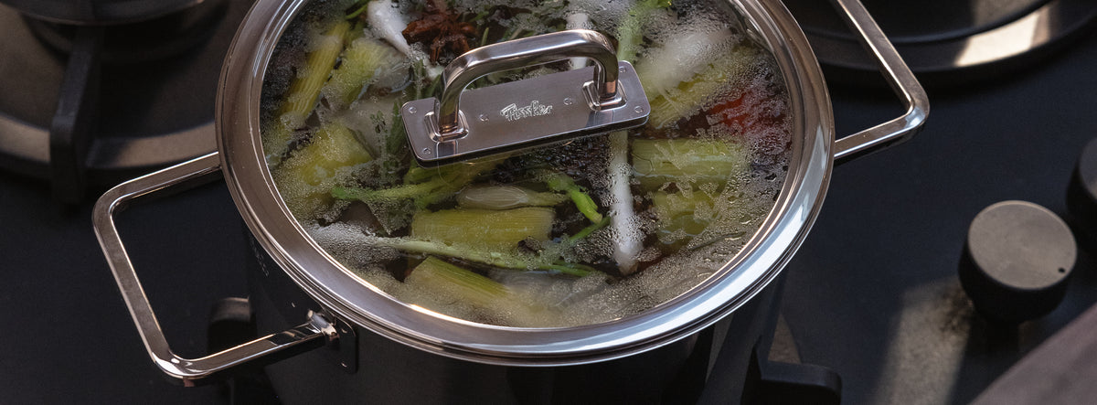 Fissler-Edelstahltopf mit Glasdeckel auf dem Herd, Präzisionsarbeit aus Deutschland, köchelt Gemüse mit sichtbarem Kondenswasser.