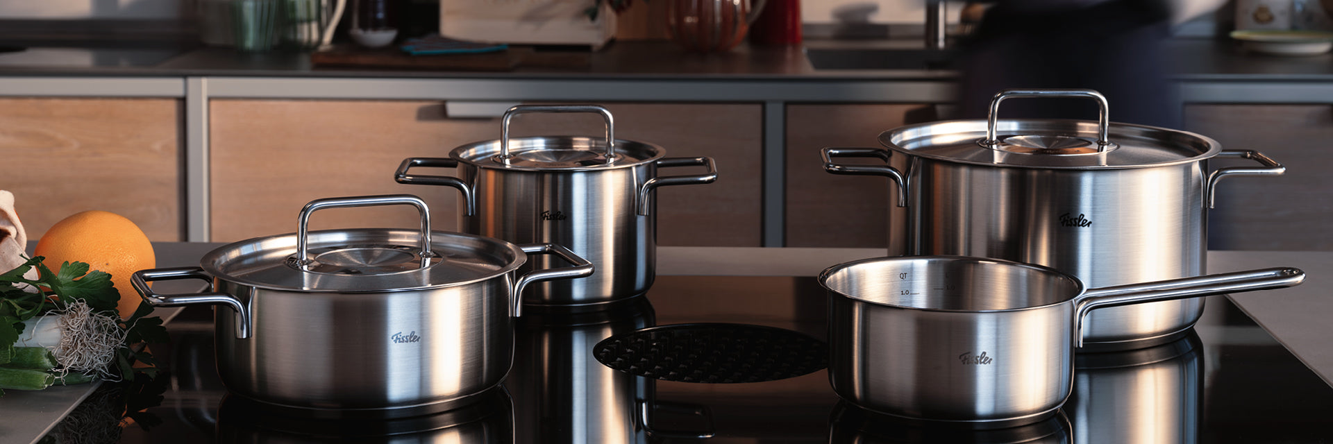 Fissler Edelstahltöpfe und -pfannen mit Deckeln auf einem modernen Herd, der deutsche Präzision und zeitloses Design in Ihrer Küche verkörpert.