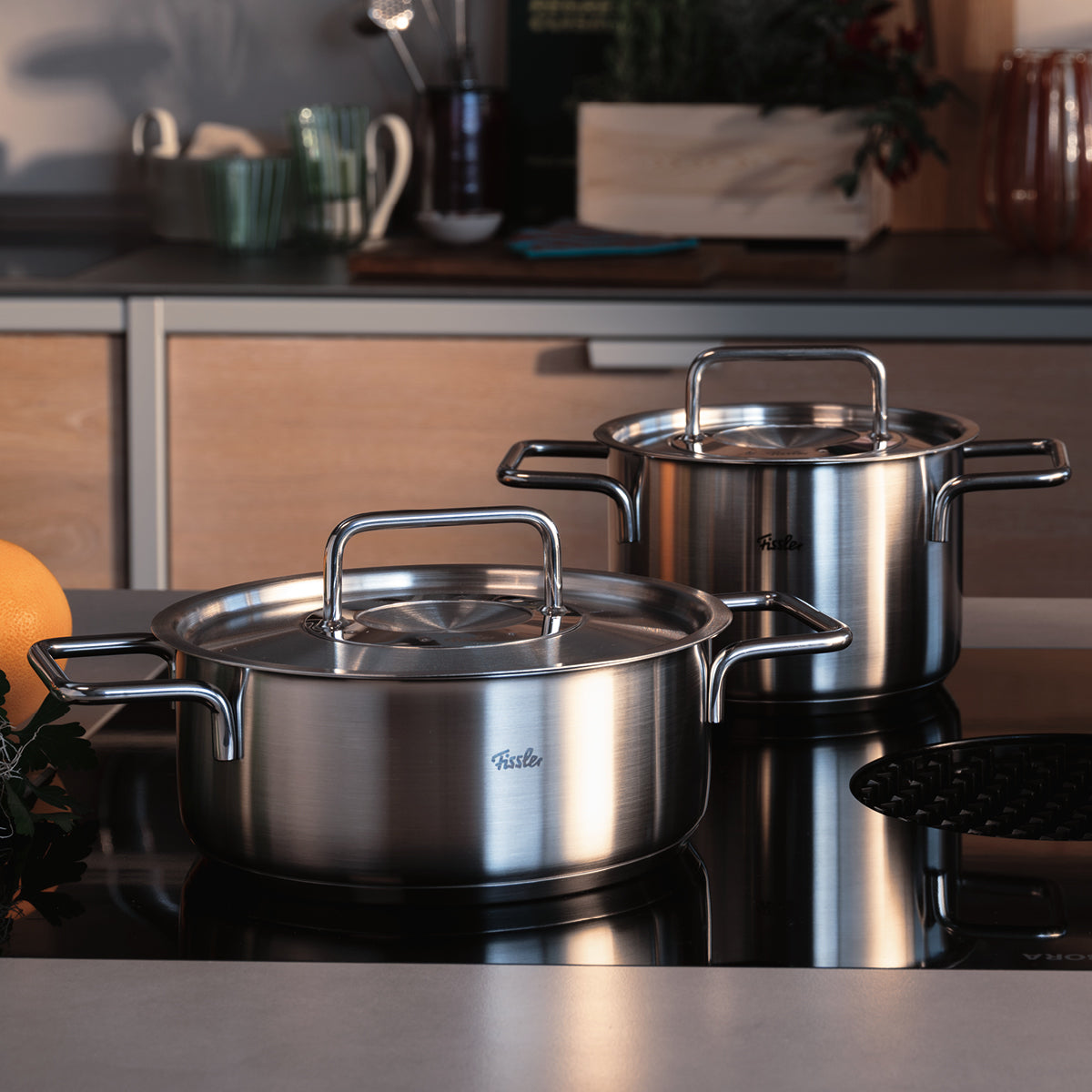 Fissler Edelstahltöpfe mit Deckel und Griffen auf einer Herdplatte, die deutsche Präzision und zeitloses Küchendesign demonstrieren.