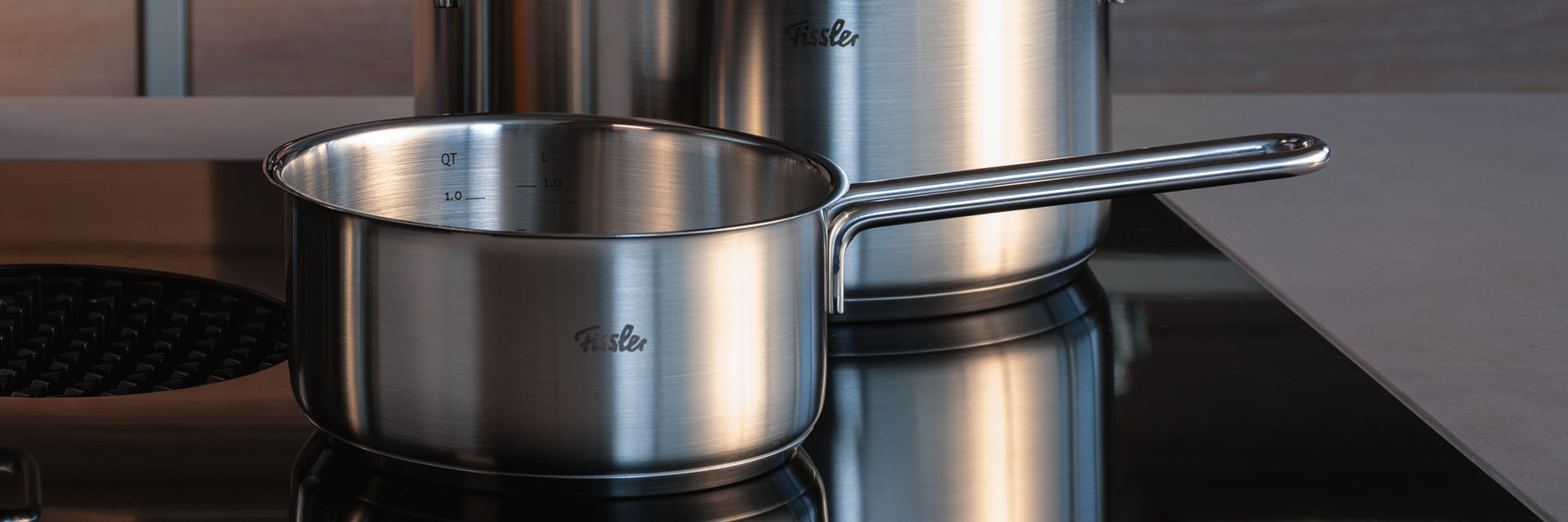 Eine in Deutschland gefertigte Fissler-Edelstahlkasserolle und ein Topf stehen auf einer Glasplatte - Präzision, Langlebigkeit und zeitloses Design.