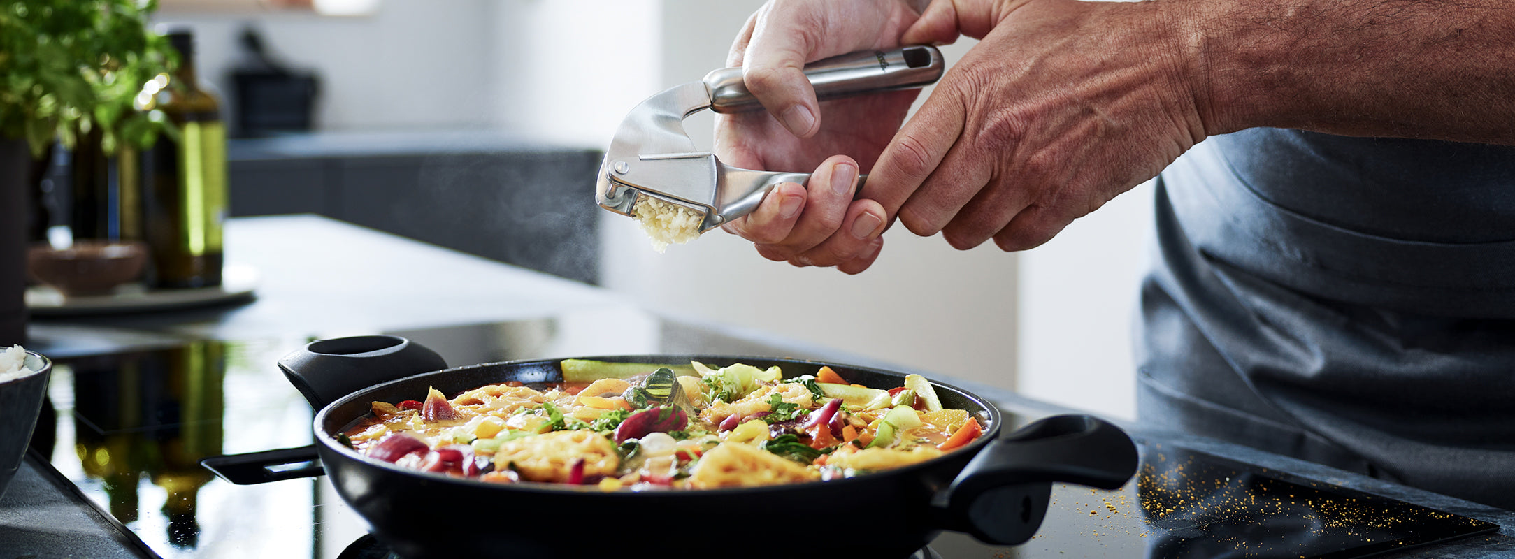 In einer schwarzen Fissler-Pfanne auf einer modernen Herdplatte wird frischer Knoblauch zu einem lebendigen Pfannengericht gepresst, das deutsche Qualität zeigt.