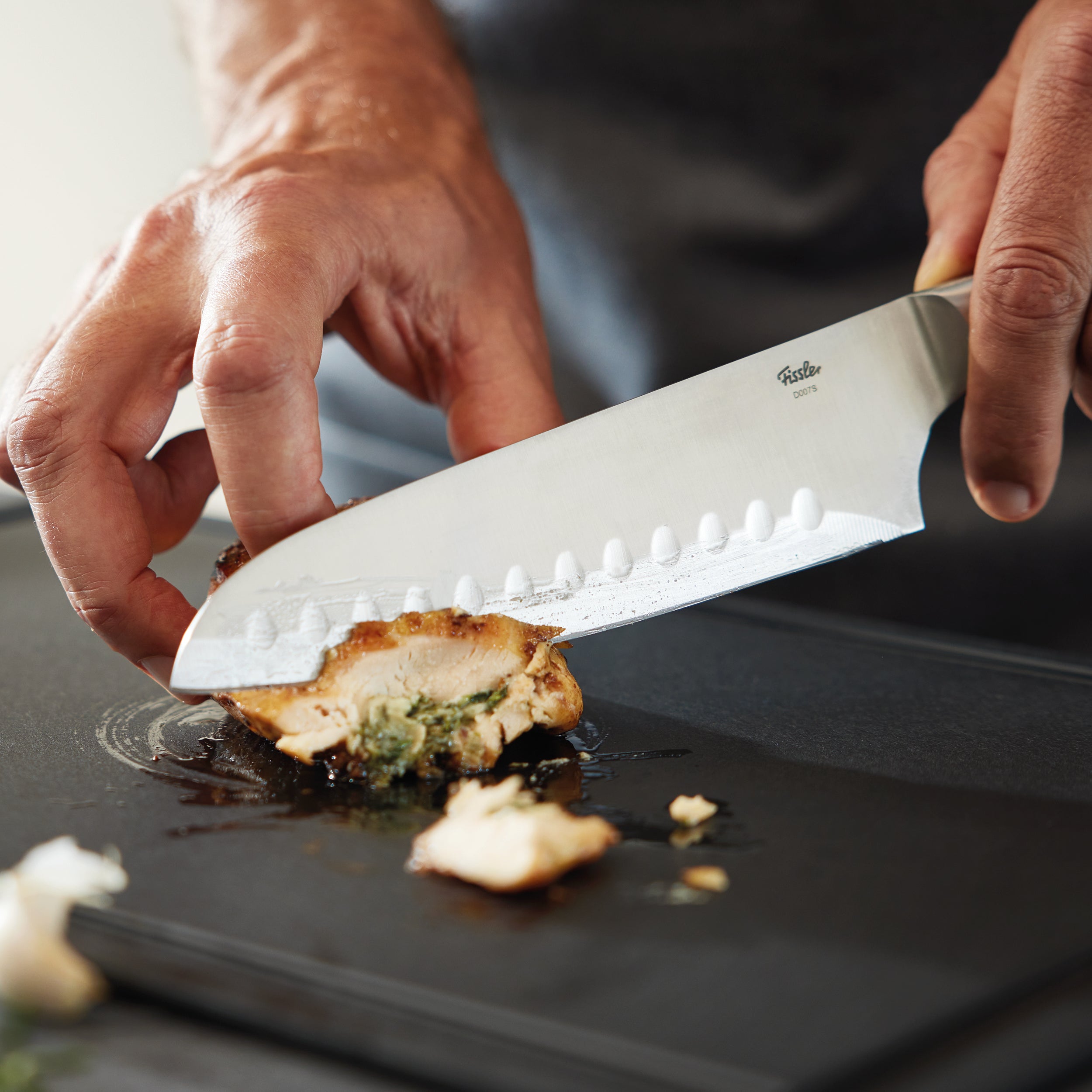 Ein Fissler Küchenmesser schneidet mühelos gekochte Hähnchenbrust auf einem glatten Schneidebrett, das Präzision und zeitlose Qualität widerspiegelt.