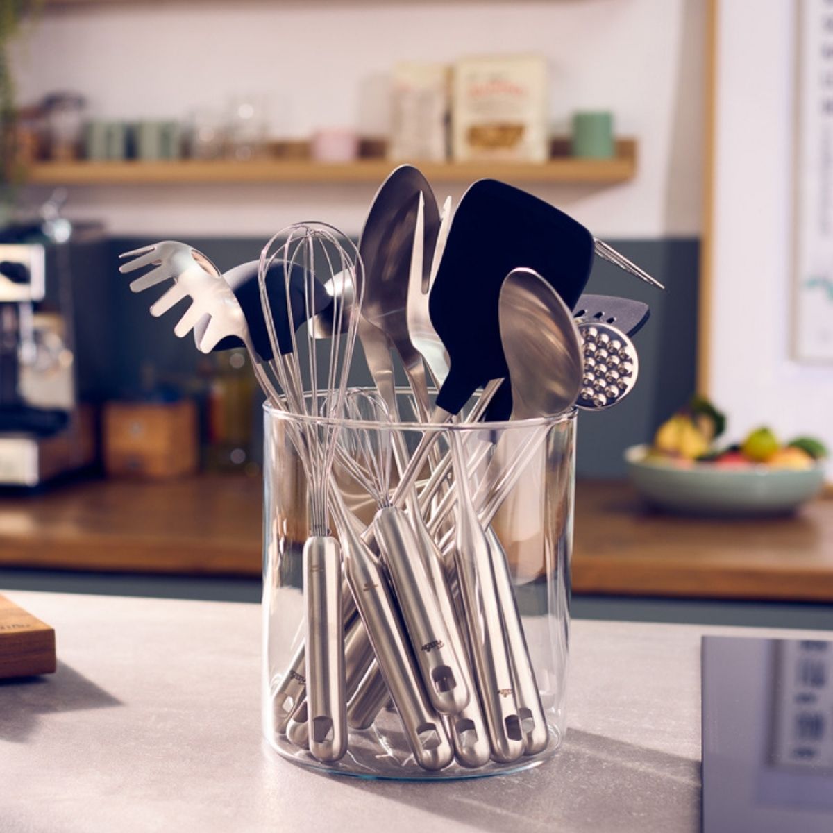 Hochwertige Fissler-Edelstahl-Utensilien in einem durchsichtigen Halter auf einer Küchentheke, der deutsche Präzision und zeitloses Design widerspiegelt.