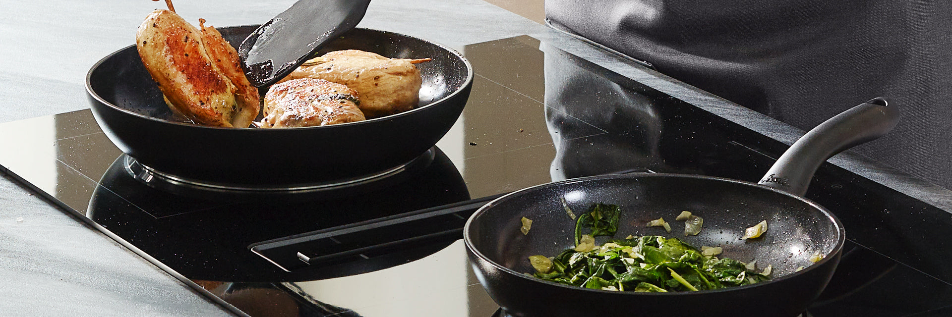 Ein Koch kocht Hähnchenbrust und sautiert Grünzeug mit Zwiebeln in Fissler-Edelstahlpfannen auf einem eleganten schwarzen Induktionskochfeld.