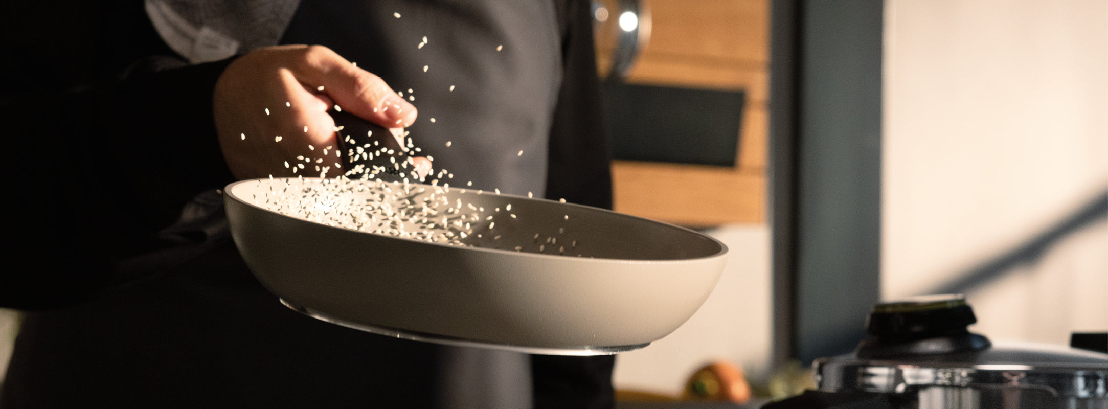 Ein Koch schwenkt fachmännisch Reis in einer Fissler-Edelstahlpfanne und stellt damit Präzision und Innovation in einer modernen Küche unter Beweis.