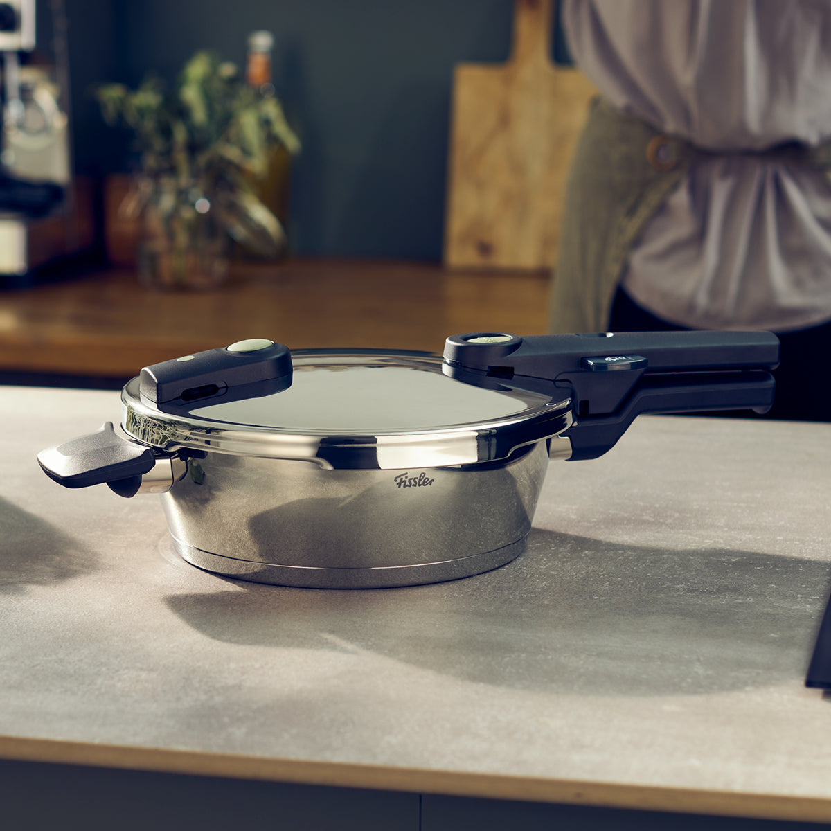 Auf der Küchentheke steht ein Fissler Schnellkochtopf aus Edelstahl mit schwarzen Griffen, gefertigt mit deutscher Präzision und zeitlosem Design.