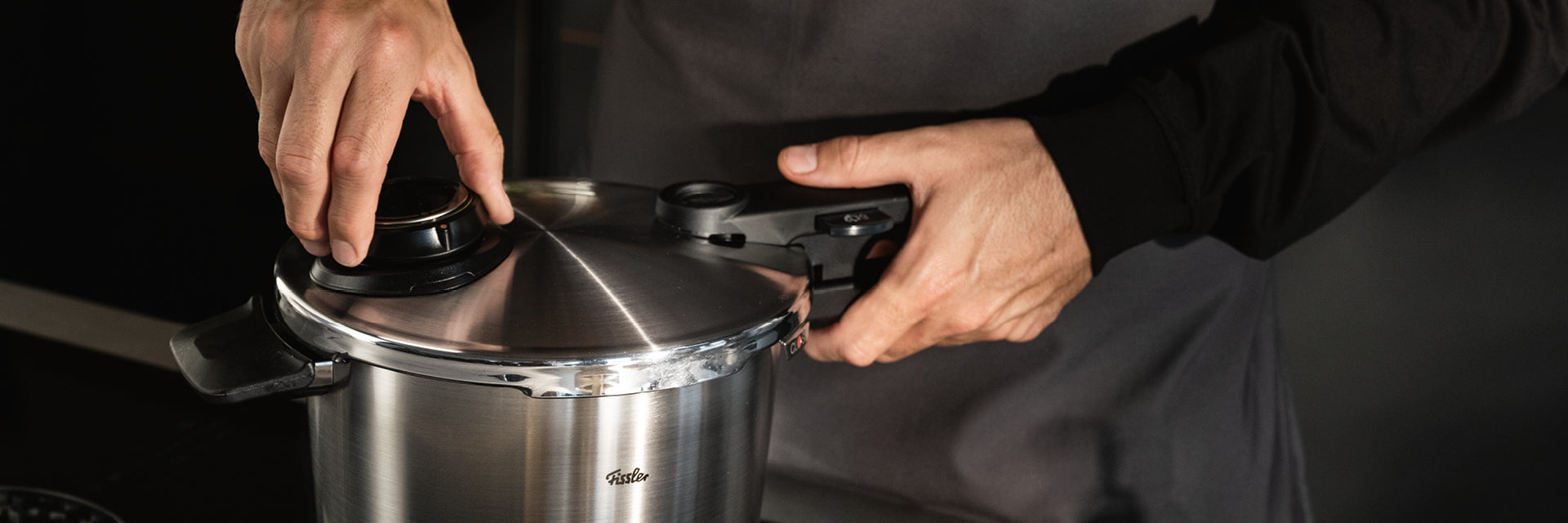 Eine Person in dunklem Hemd und Schürze verschließt den Deckel eines Fissler-Edelstahl-Schnellkochtopfs und demonstriert damit deutsche Präzision in der Küche.