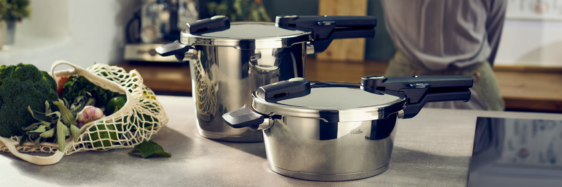 Fissler-Edelstahl-Schnellkochtöpfe auf einer Küchentheke neben frischem Gemüse - ein Erbe deutscher Qualität und deutschen Designs.
