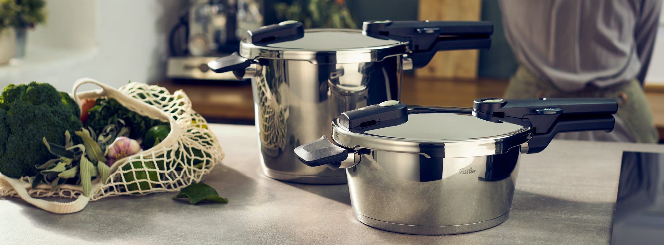 Fissler Schnellkochtöpfe aus rostfreiem Stahl mit schwarzen Griffen auf einer Küchentheke, gepaart mit frischem Gemüse in einer hellen Umgebung.