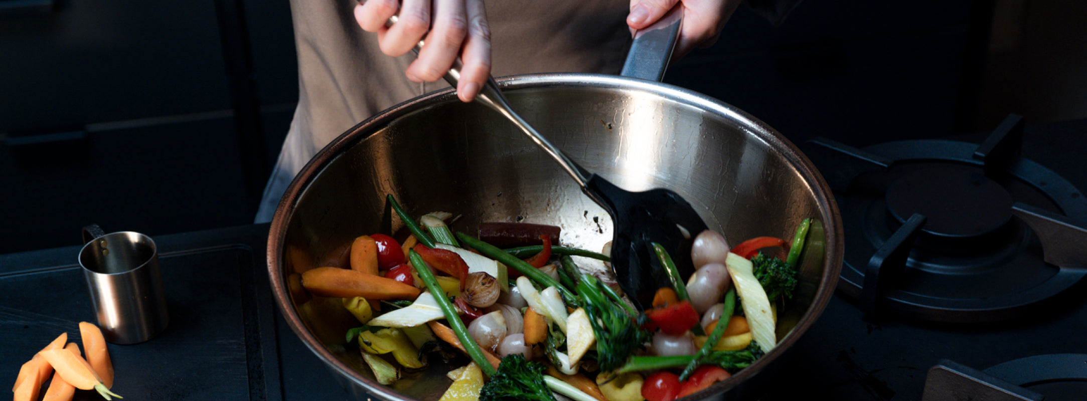 Eine Person rührt mit einem schwarzen Pfannenwender lebendiges Gemüse in einer Fissler-Edelstahlpfanne, die deutsche Qualität und deutsches Design demonstriert.