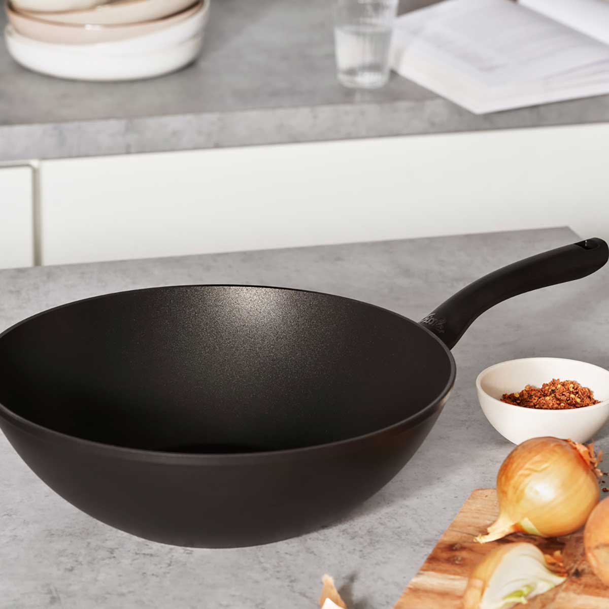 Fissler Cenit® Wok Pan Induction 28 cm - Precision and Design. Surrounded by spices, water, cookbook, and cutting board.