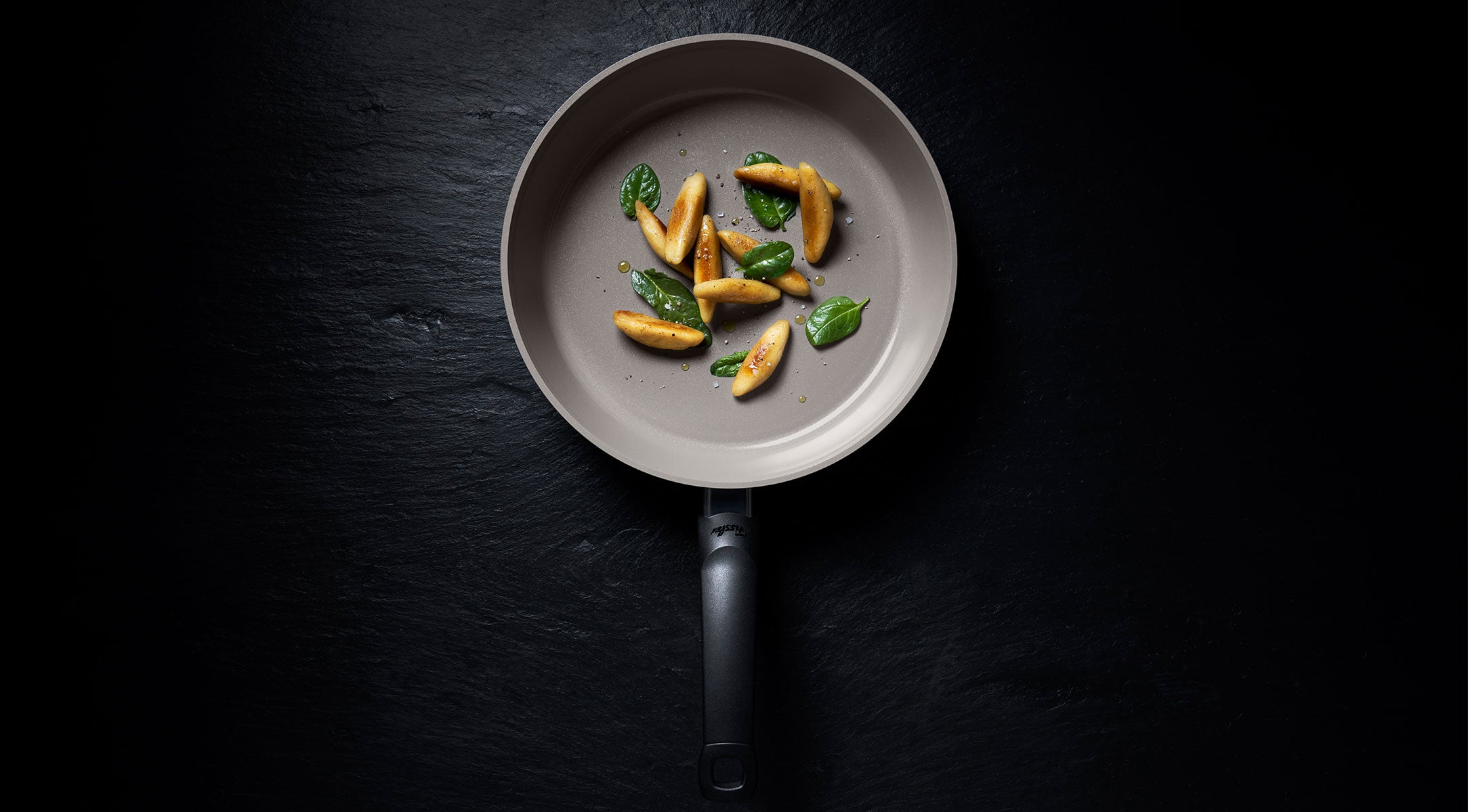 Fissler Antihaft-Pfanne auf dunkler Oberfläche mit goldbraunen Gnocchi und Basilikum, die von deutscher Präzision und zeitlosem Design zeugt.