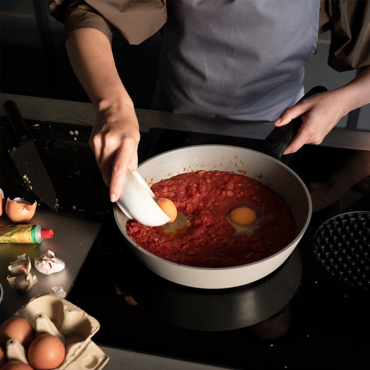 Erleben Sie präzises Kochen mit den Fissler Ceratal® Evo Comfort-Pfannen, während Eier in die Tomatensoße geschlagen werden, umgeben von frischen Zutaten.