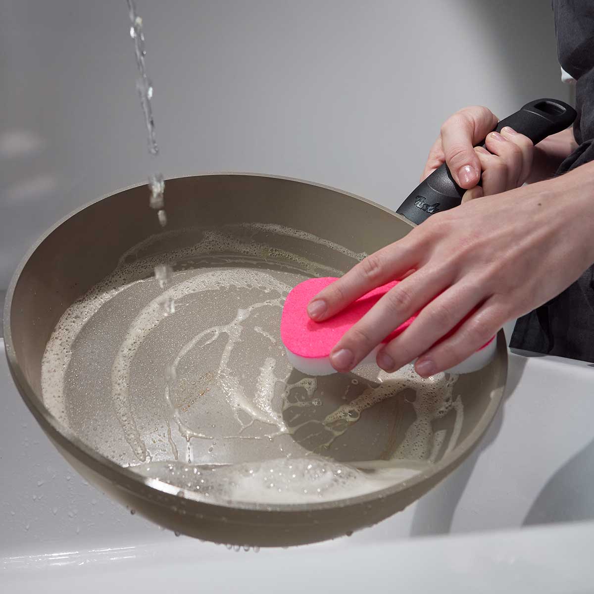 Cleaning the Fissler Ceratal® Comfort Frying Pan 26cm with Glass Lid under running water highlights its easy-care, high-quality design.