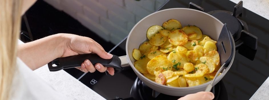 Eine Person kocht goldbraune Kartoffeln mit Kräutern in einer Fissler-Pfanne auf einem eleganten schwarzen Herd und zeigt damit deutsche Präzision.