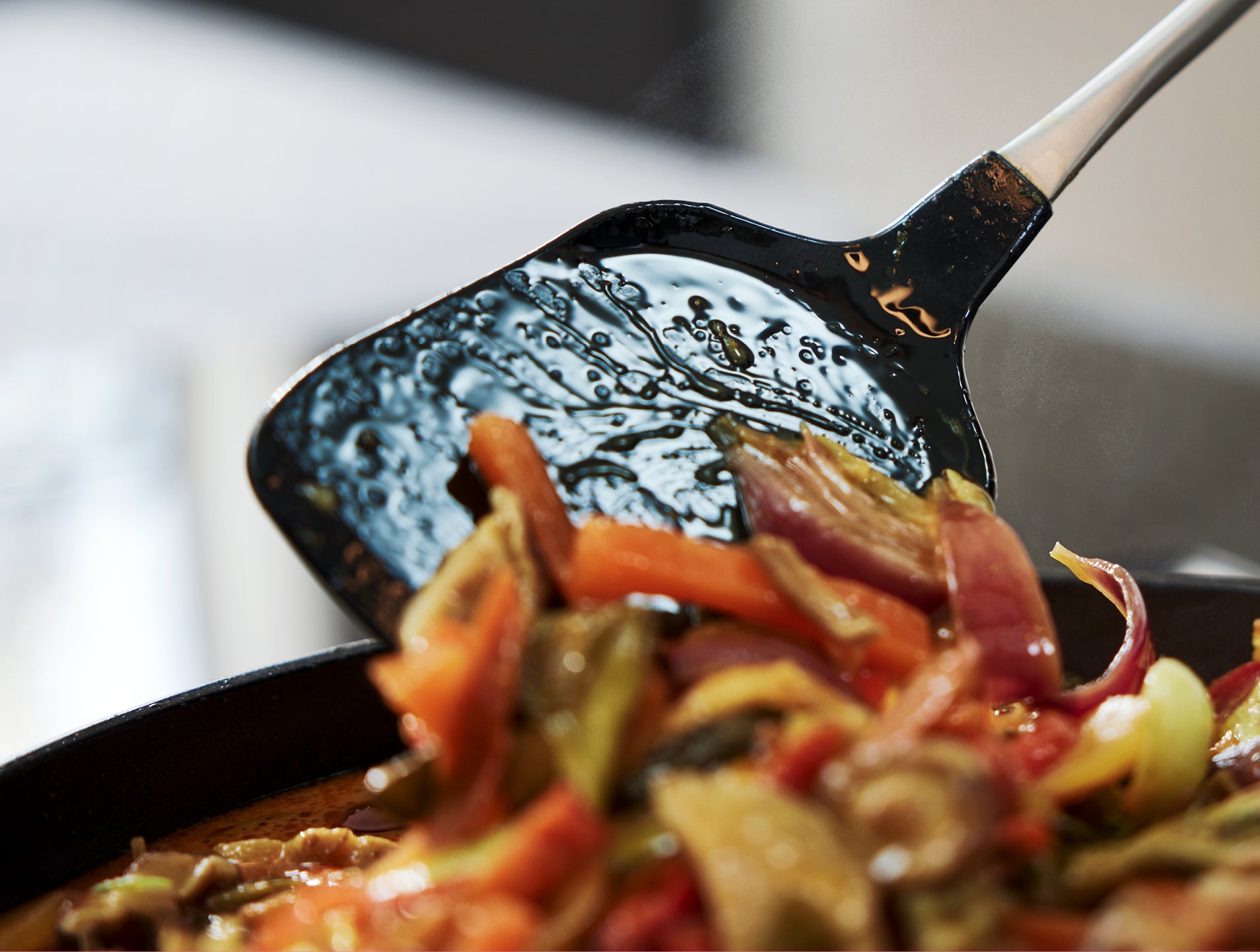 Ein Fissler Pfannenwender hebt lebendig gebratenes Gemüse aus einer Fissler Pfanne, Dampf steigt auf - deutsches Präzisionskochgeschirr im Einsatz.