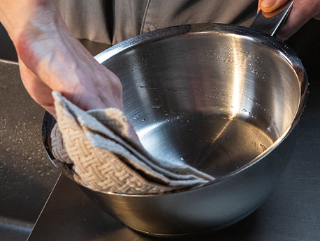 Eine Person reinigt sanft einen Fissler-Edelstahltopf mit einem beigen Tuch und zeigt damit die Präzision und dauerhafte Qualität der Marke.