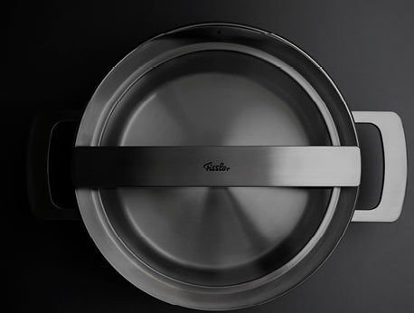 Eine Draufsicht auf einen Fissler-Edelstahltopf mit schwarzen Griffen. Der Deckel in der Mitte trägt das ikonische Logo, das deutsche Handwerkskunst symbolisiert.