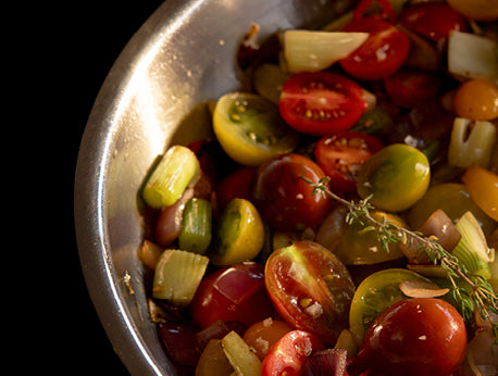 Eine Fissler-Edelstahlschüssel mit leuchtenden Kirschtomaten, Sellerie, Zwiebeln und Thymian - ein Beispiel für deutsche Präzision und Qualität.