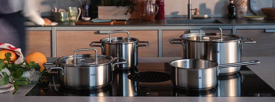 Fissler Töpfe und Pfannen aus rostfreiem Stahl mit Deckel auf einem eleganten Induktionsherd, der deutsche Präzision und zeitloses Design verkörpert.
