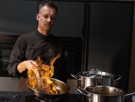 Ein Koch in einer modernen Küche verwendet Töpfe und eine Pfanne aus rostfreiem Stahl von Fissler und stellt damit Präzision und deutsches Qualitätskochgeschirr unter Beweis.