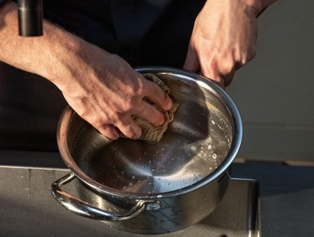 Die Hände reinigen vorsichtig einen Fissler-Edelstahltopf unter fließendem Wasser, wobei die Seifenlauge die makellose deutsche Handwerkskunst hervorhebt.