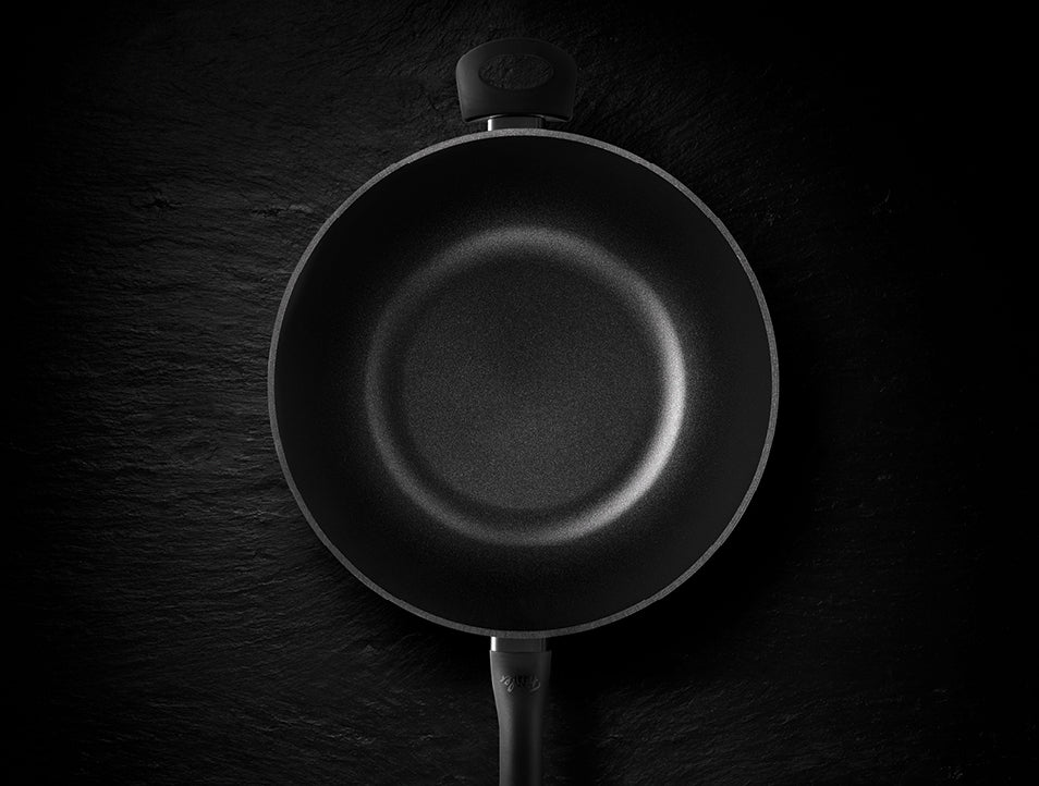 Eine in Deutschland hergestellte antihaftbeschichtete Bratpfanne von Fissler, von oben gesehen auf einer dunklen Fläche mit elegant nach unten gerichtetem Griff.