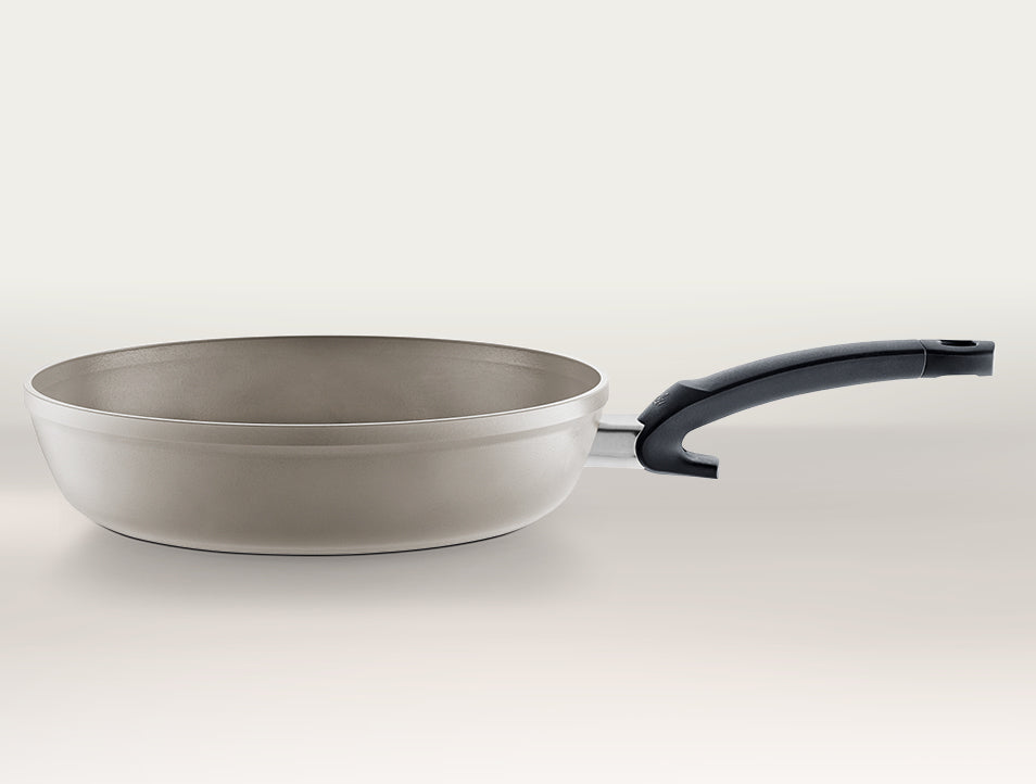 Fissler antihaftbeschichtete Bratpfanne mit hellgrauem Äußeren und schwarzem ergonomischen Griff, hergestellt in Deutschland, abgebildet auf einem einfarbigen Hintergrund.