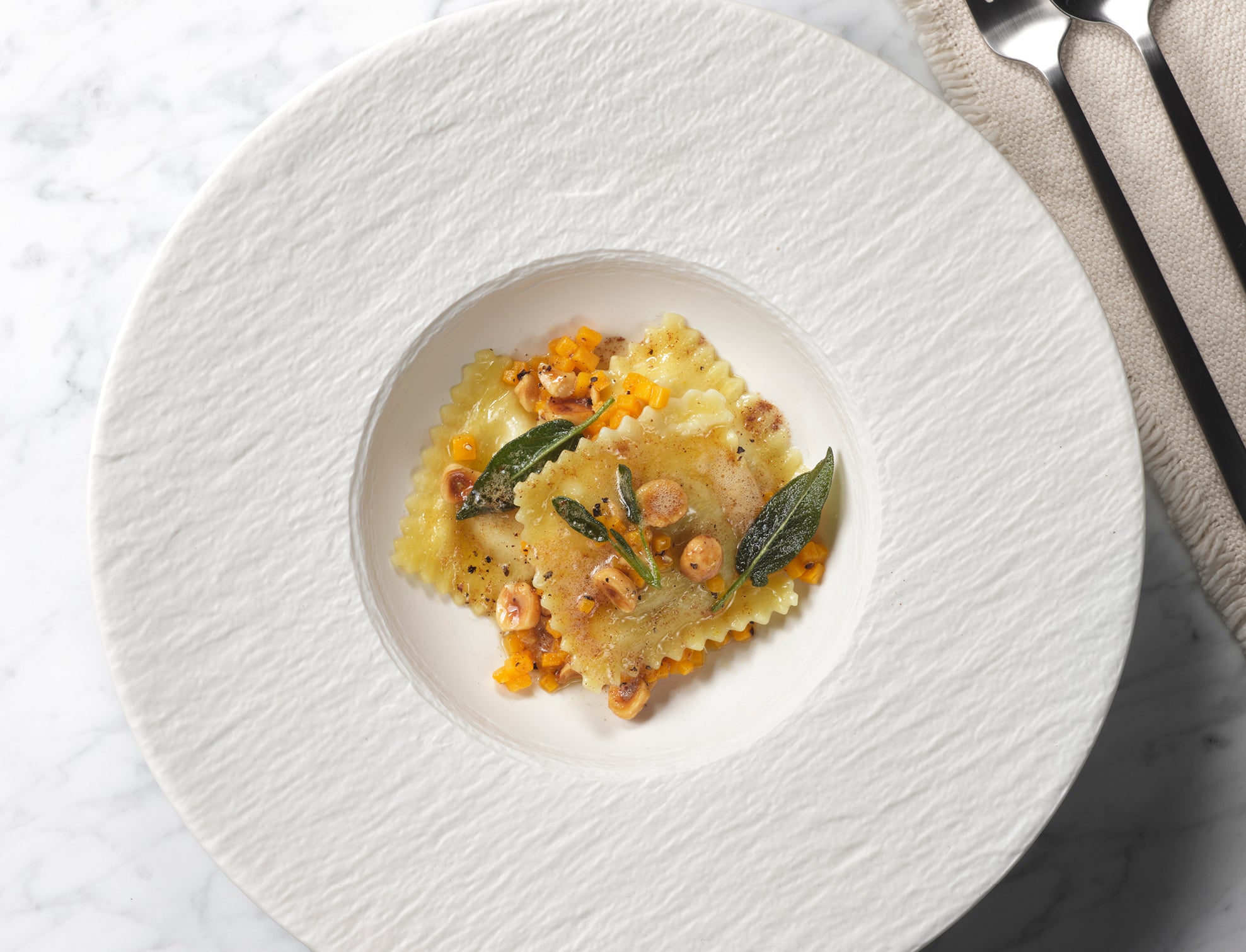 Fachmännisch zubereitete Ravioli mit brauner Butter, Salbei, Mais und Haselnüssen auf Marmor und mit Besteck, das mit Fissler-Kochgeschirr hergestellt wurde.
