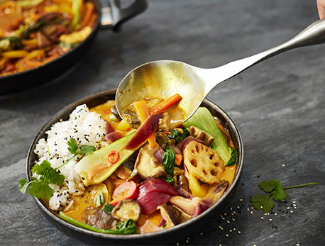 Ein lebhaftes Gemüsecurry mit Reis, serviert in hochwertigem Kochgeschirr. Ein handgehobenes Curry mit einem Löffel - frisch, farbenfroh und fachmännisch zubereitet.