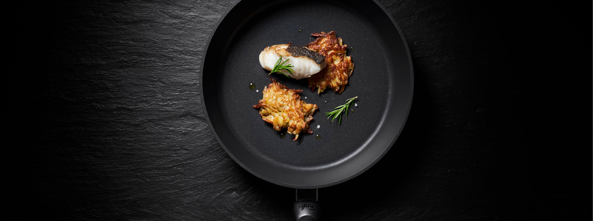 Eine Fissler Premium-Bratpfanne mit gekochtem Fisch, frischen Kräutern und goldenen Kartoffelrösti, die deutsche Qualitätsarbeit zeigt.