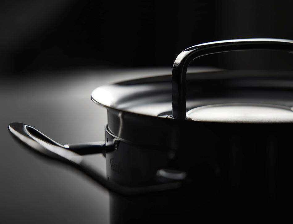 Die Nahaufnahme eines Fissler-Edelstahltopfs mit Deckel und Griffen, der im Licht schimmert, zeigt deutsche Präzision und zeitloses Design.