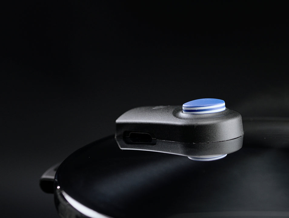 Nahaufnahme eines Fissler-Schnellkochtopfdeckels mit dem charakteristischen schwarz-blauen Ventil, das in Deutschland entwickelt wurde. Im Hintergrund tritt leise Dampf aus.