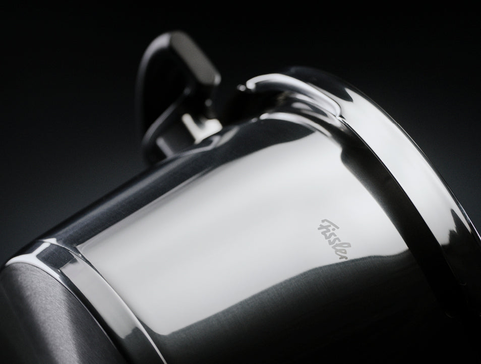 Nahaufnahme eines Fissler-Edelstahltopfs mit Griff und eingraviertem Logo, der deutsche Präzision und zeitloses Design vor einem dunklen Hintergrund zeigt.