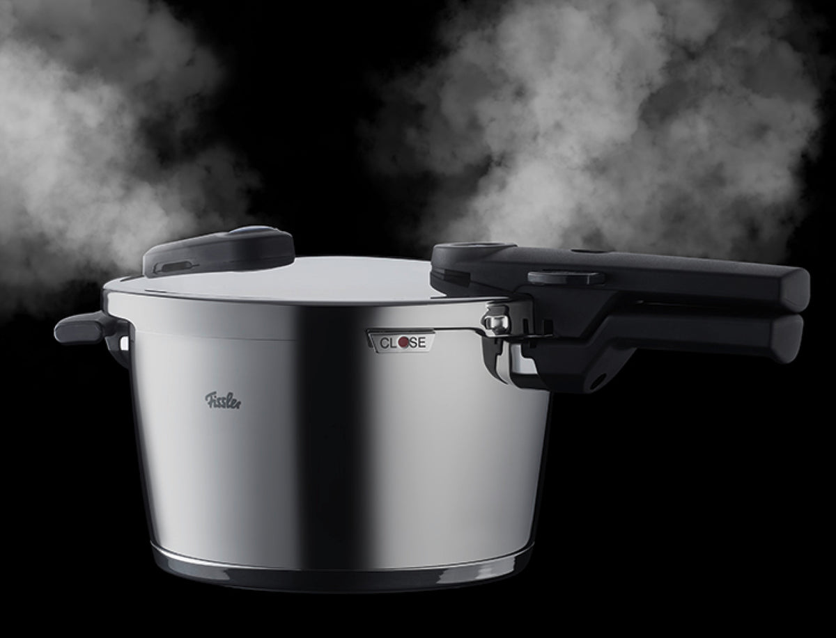 Der Fissler Edelstahl-Schnellkochtopf lässt den Dampf an den oberen Griffen ab; CLOSE am Verriegelungsmechanismus des Deckels. Zeitloses deutsches Design.