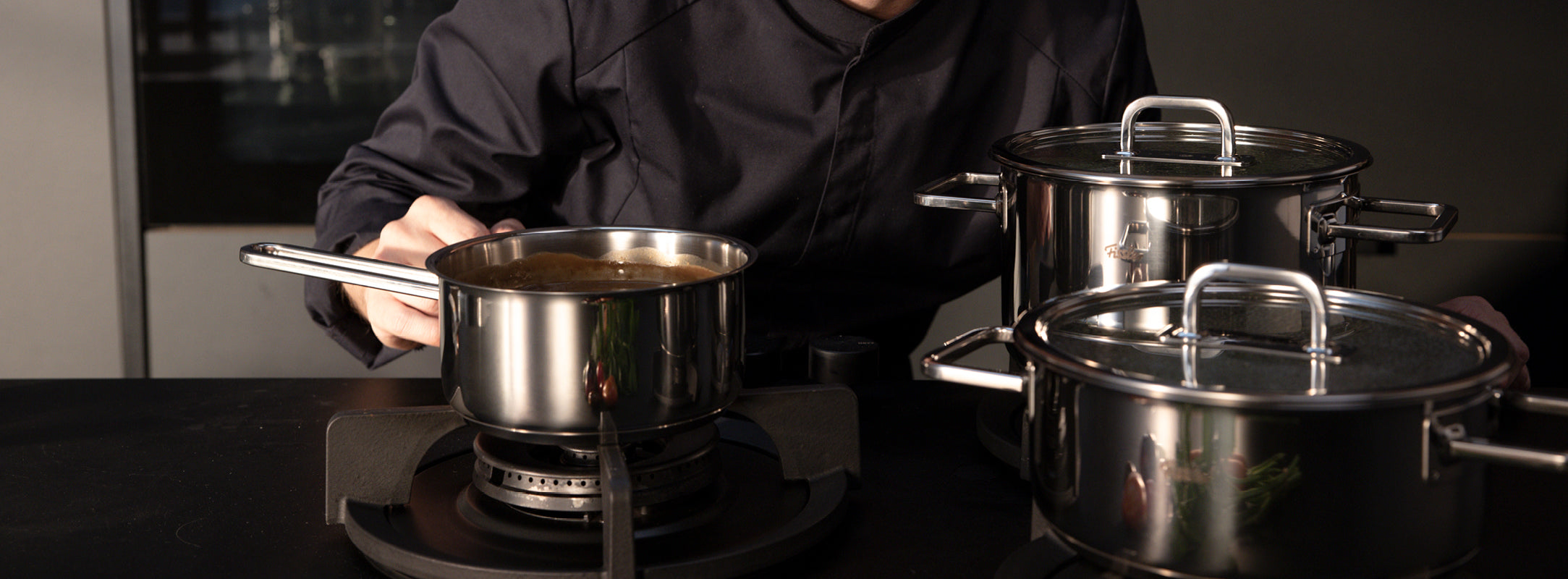 Ein Koch rührt Speisen in Fissler-Edelstahltöpfen auf einem Gasherd in einer modernen Küche, die deutsche Präzision und Design widerspiegelt.